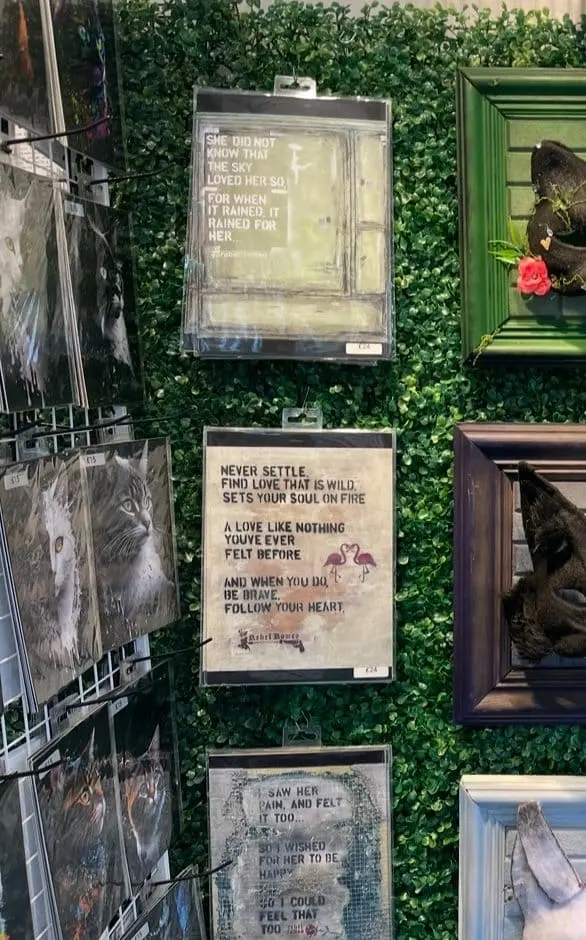 Rebel Romeo prints displayed for sale on a green-foliage gallery wall among other artists' work