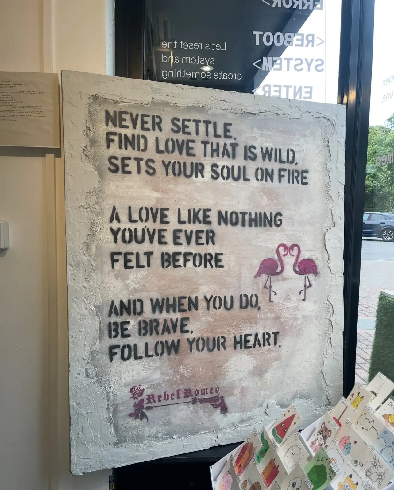 Never Settle canvas displayed in a gallery window beside vinyl lettering reading: let's reset the system and create something